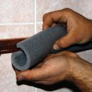 A worker fitting a layer of insulation around a copper pipe