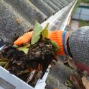 A man scoops up a pile of debris from the rain gutters that he is cleaning.